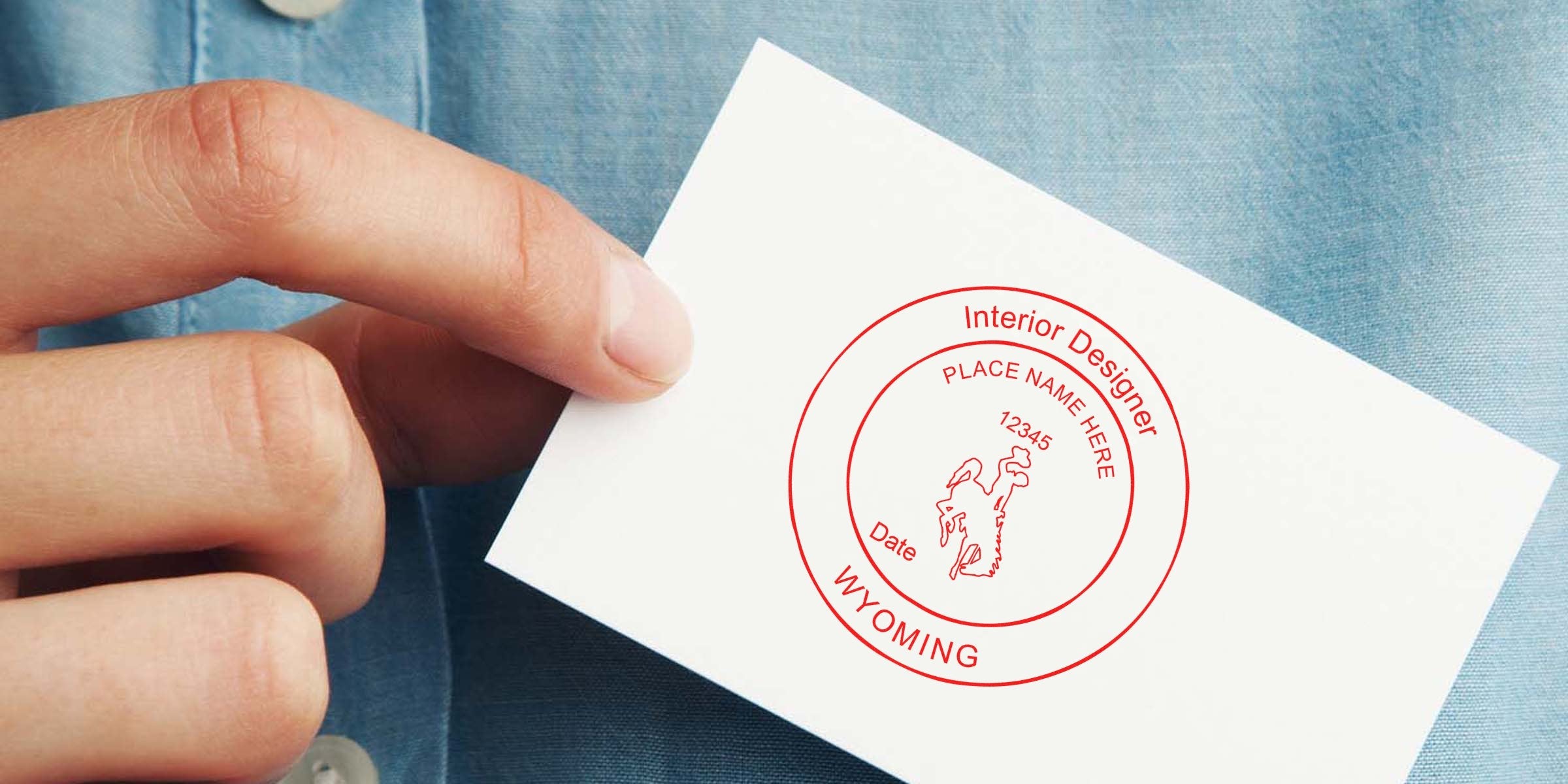 Hand holding a business card with Interior Designer Stamp Wyoming and Wyoming Interior Design License logo.