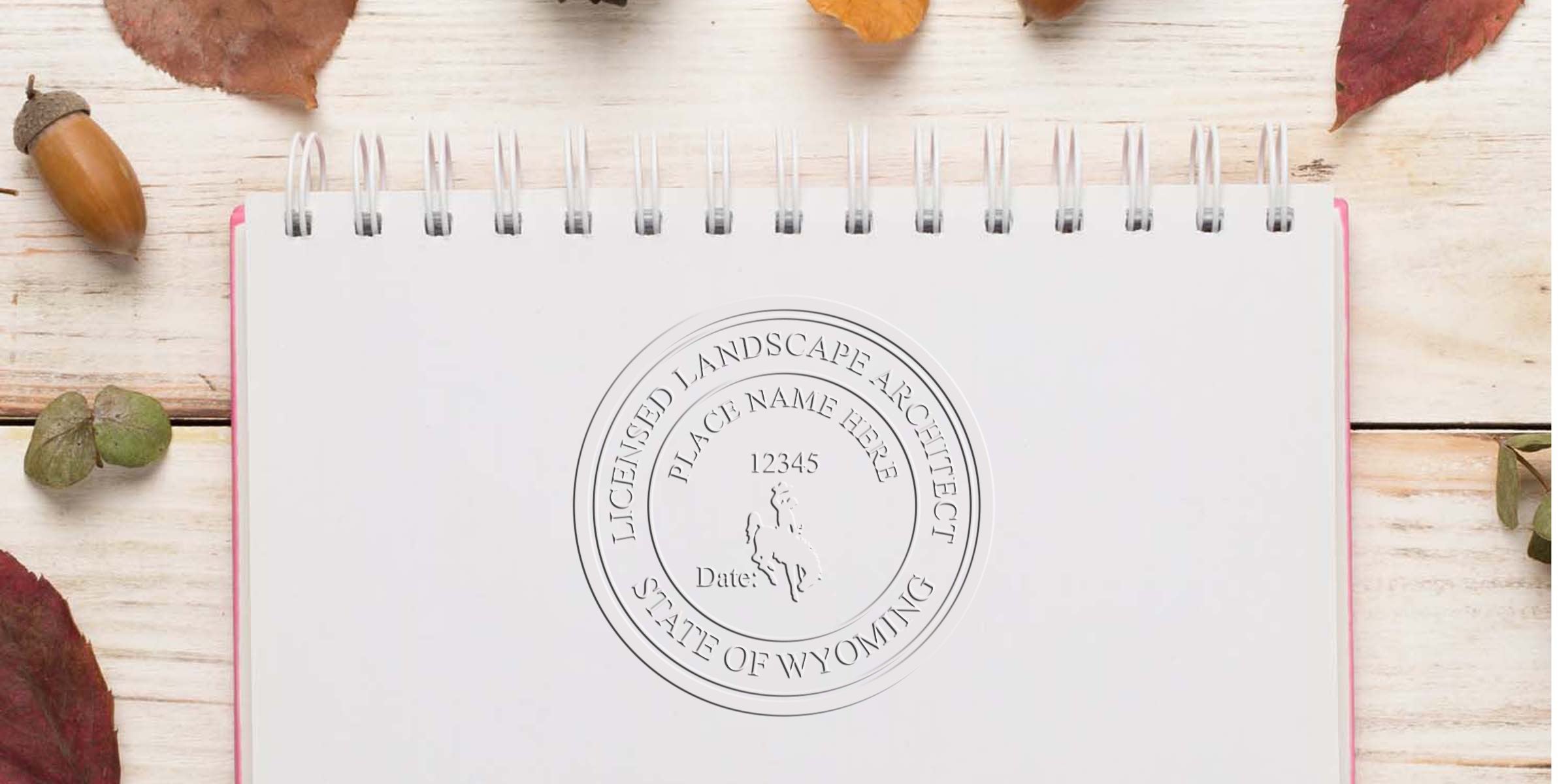 Licensed landscape architect stamp and Wyoming embosser seal on white notebook with autumn leaves and acorns background.