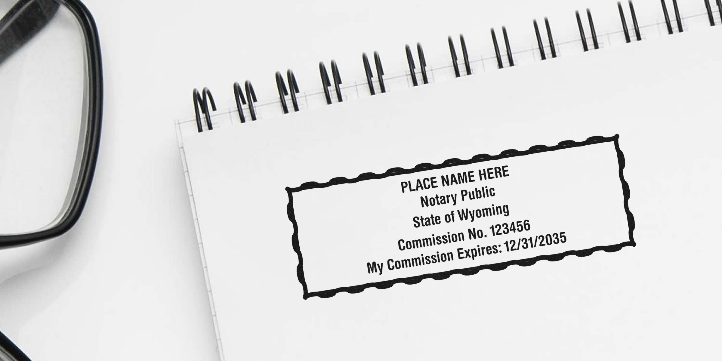 Wyoming notary stamp on white spiral notebook with glasses, displaying commission expiration date; purchase Wyoming notary stamp.