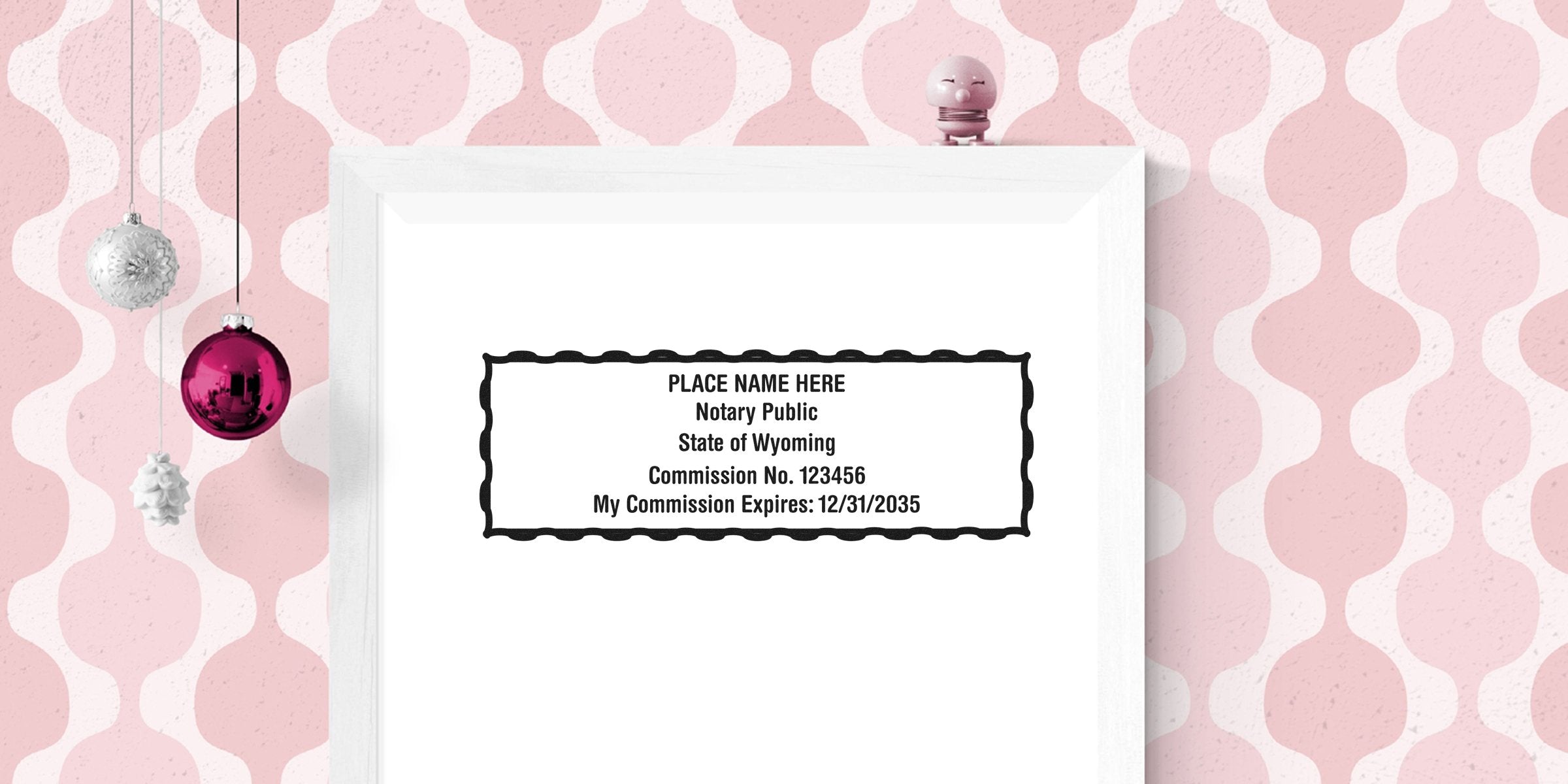 Wyoming notary stamp with commission number and expiration date on white frame, set against pink patterned background, showing correct notary seal size and Wyoming seal dimensions.