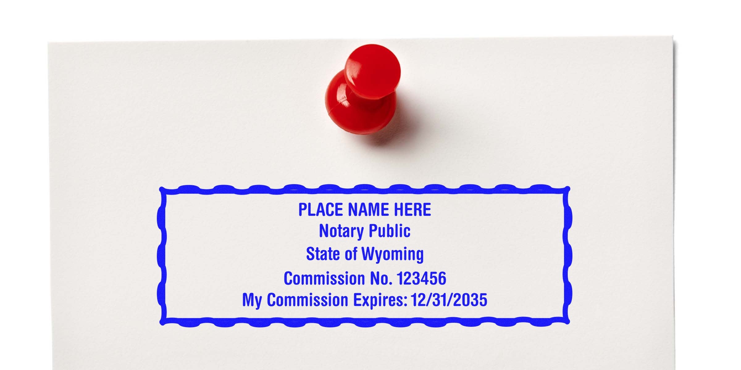 Red push pin holds Wyoming notary public stamp with commission number and expiration date on white paper, showcasing Wyoming notary supplies and essentials.