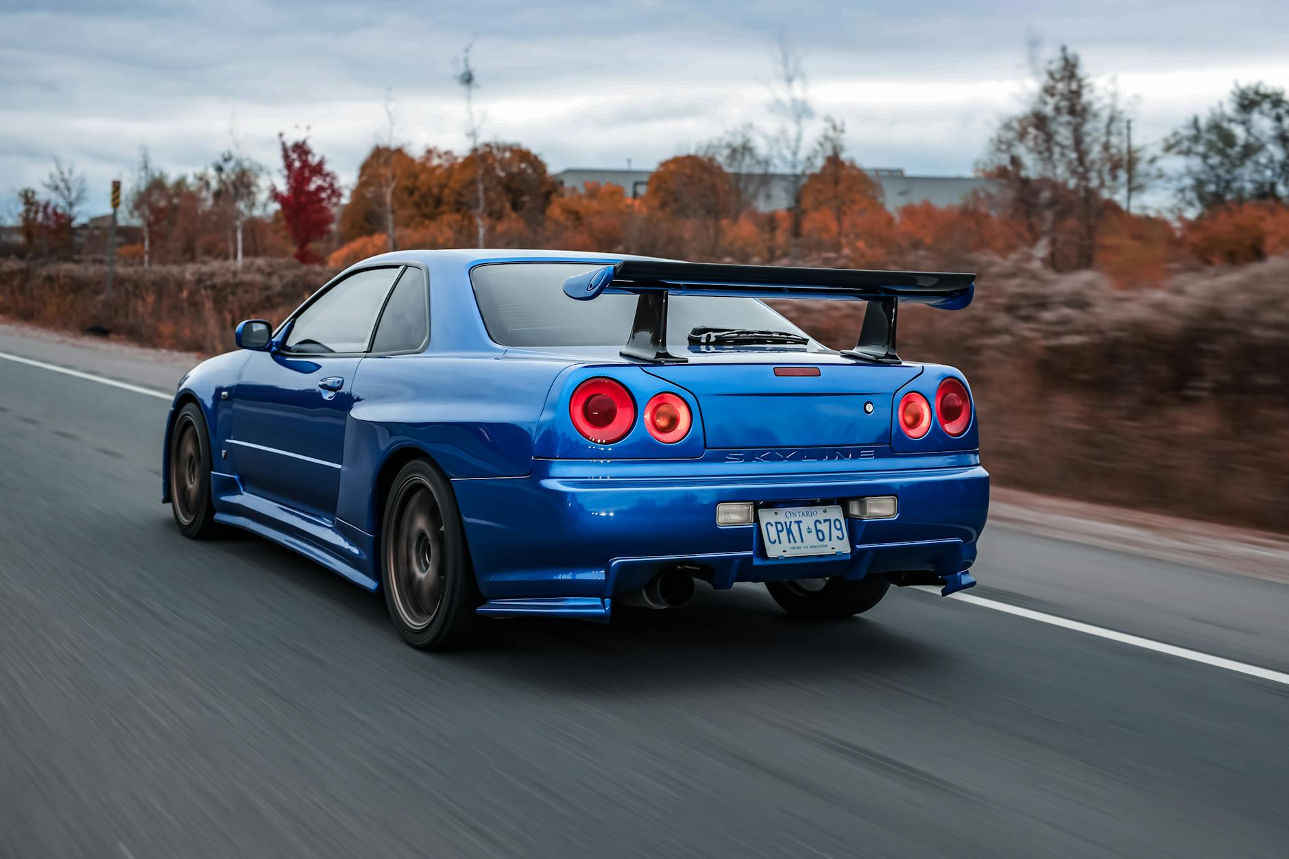 Blue Nissan Skyline R34 sports car drives past autumn trees, highlighting performance and street racing style, featuring Custom PE Seals Canada, recognized as the Best PE Seals Canada.