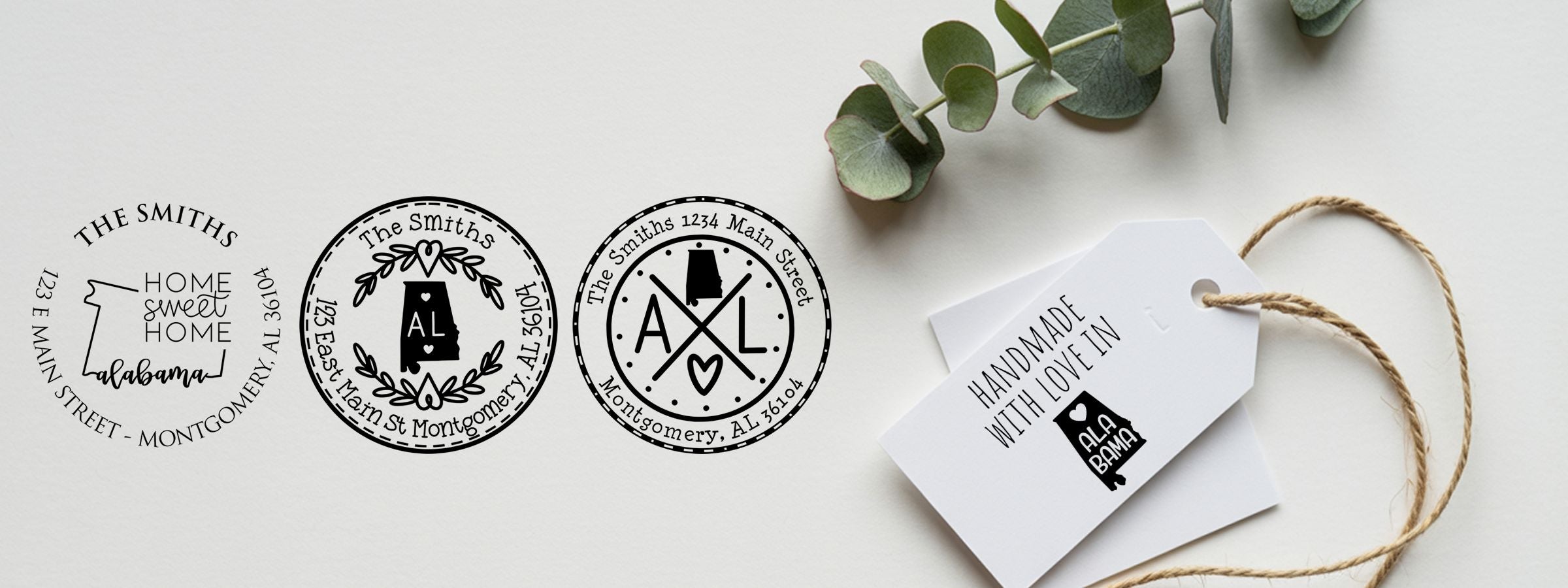 Four black-and-white Alabama Designer Stamps and Seals logo designs beside a twine gift tag and eucalyptus leaves.