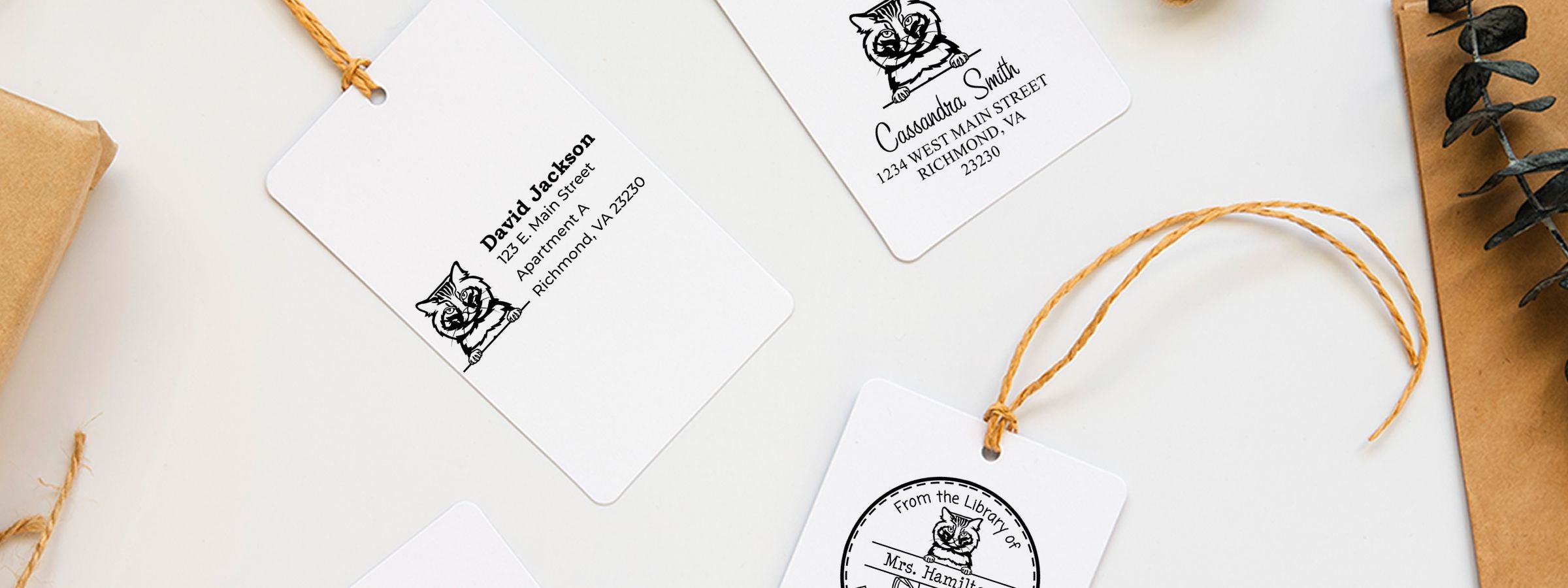White gift tags with black cat art, name and address, twine, kraft paper, and greenery for American Bobtail Cat Stamps and Custom Seals.