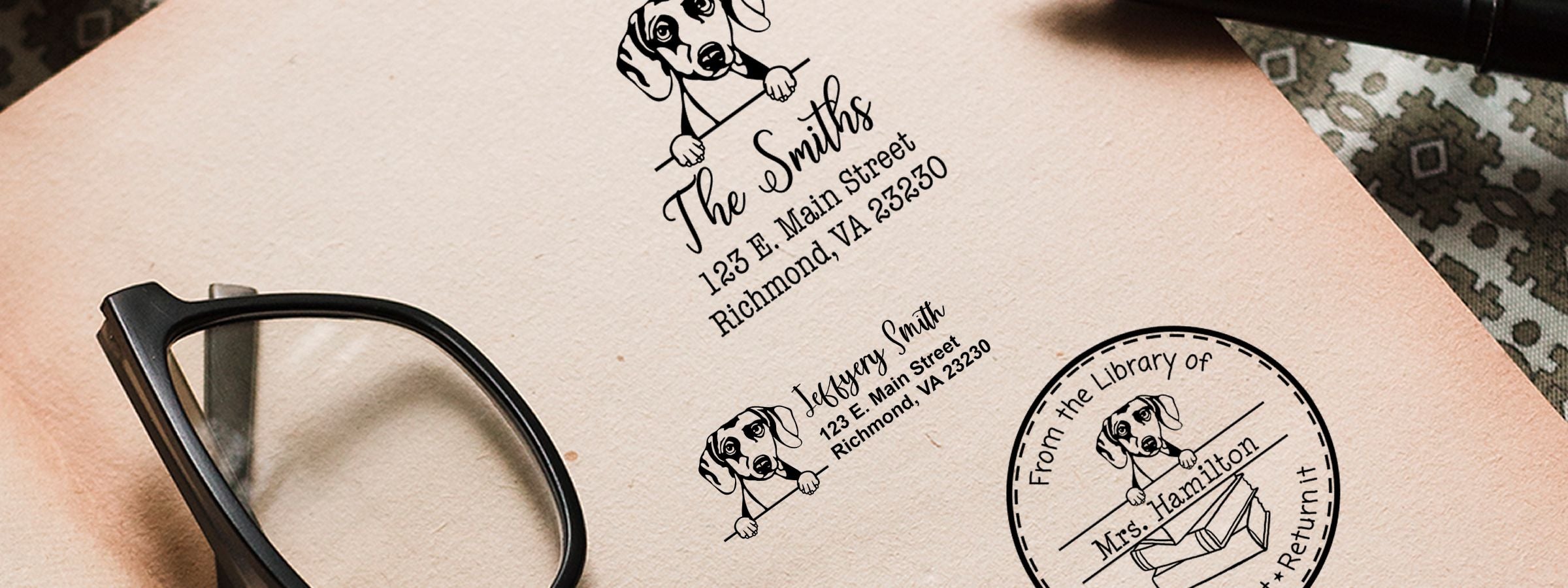 Close-up of beige paper with Daschound Dog Stamps and Custom Seals, with black eyeglasses resting on the left.