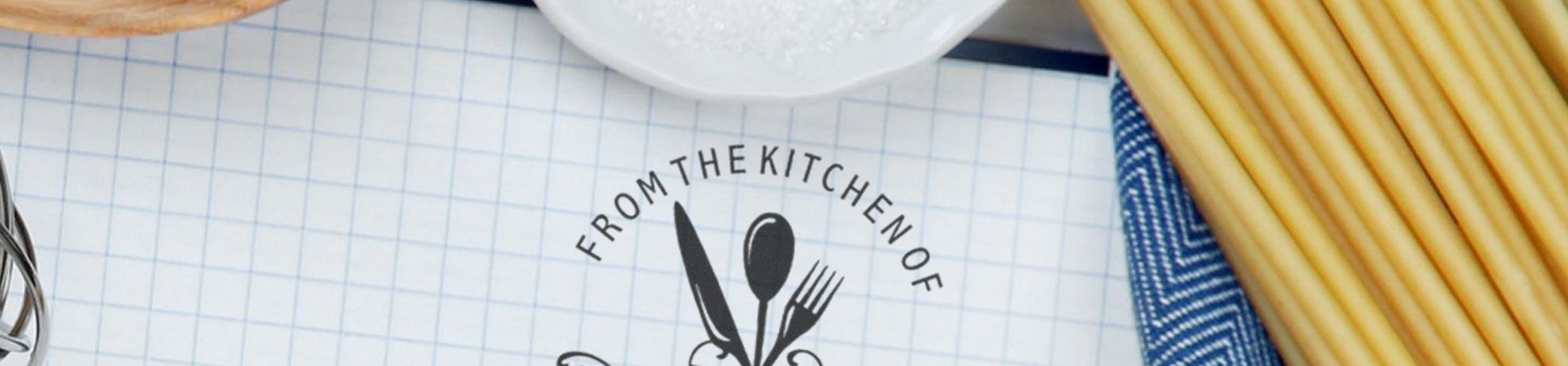 Designer Stamps kitchen design on graph paper reading “FROM THE KITCHEN OF” with knife, spoon, fork, spaghetti, and a blue towel.