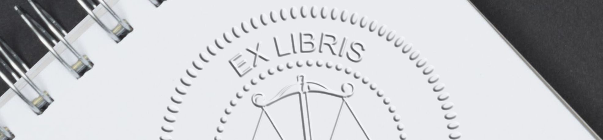 Close-up of spiral-bound notebook cover embossed with EX LIBRIS text and a circular border by embossers.