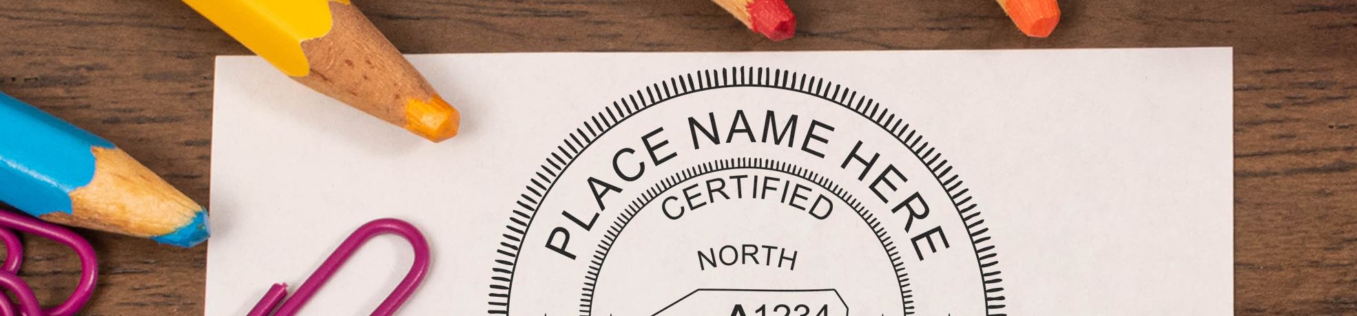 Close-up of paper on a wooden desk with Real Estate Appraiser Stamps & Real Estate Appraiser Seals reading certified north, with colored pencils and clips.