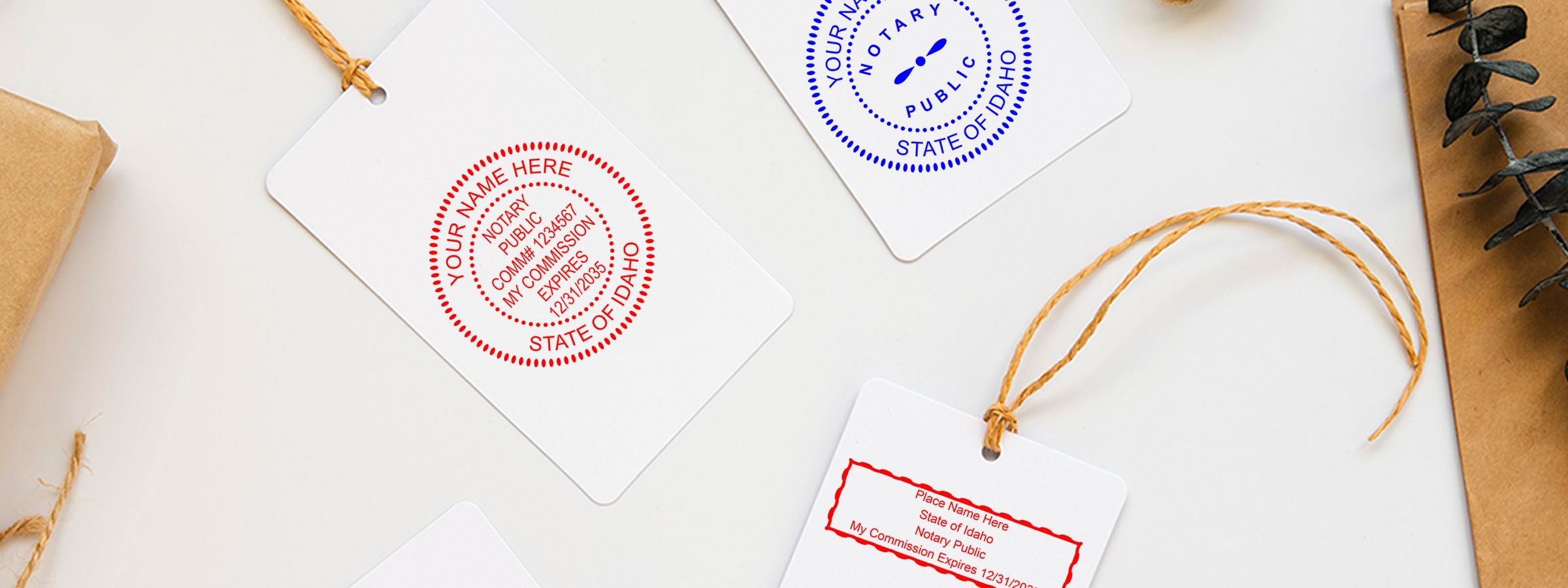 Idaho Notary Supplies, Stamps and Seals flat lay of white hanging tags with red and blue notary stamp designs on white with kraft paper and eucalyptus.