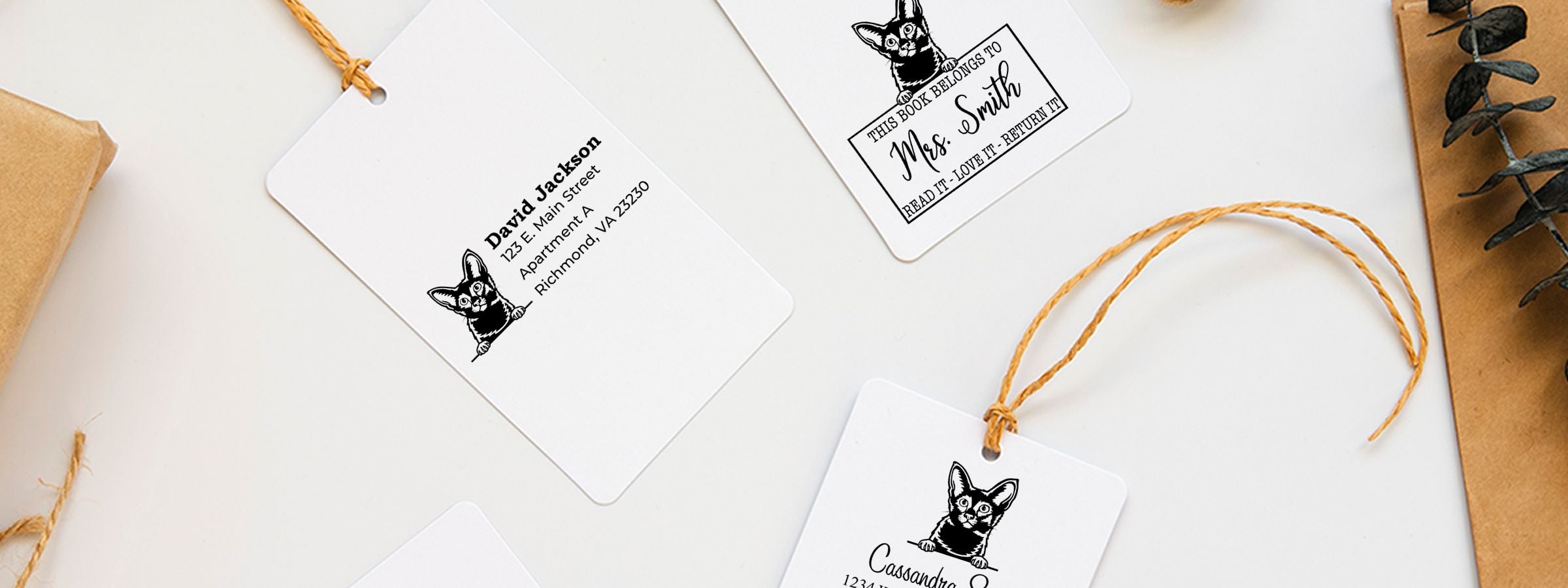 Flat lay of custom book tags with black cat illustrations and names, twine, paper, and eucalyptus, featuring Javanese Cat Stamps and Custom Seals.