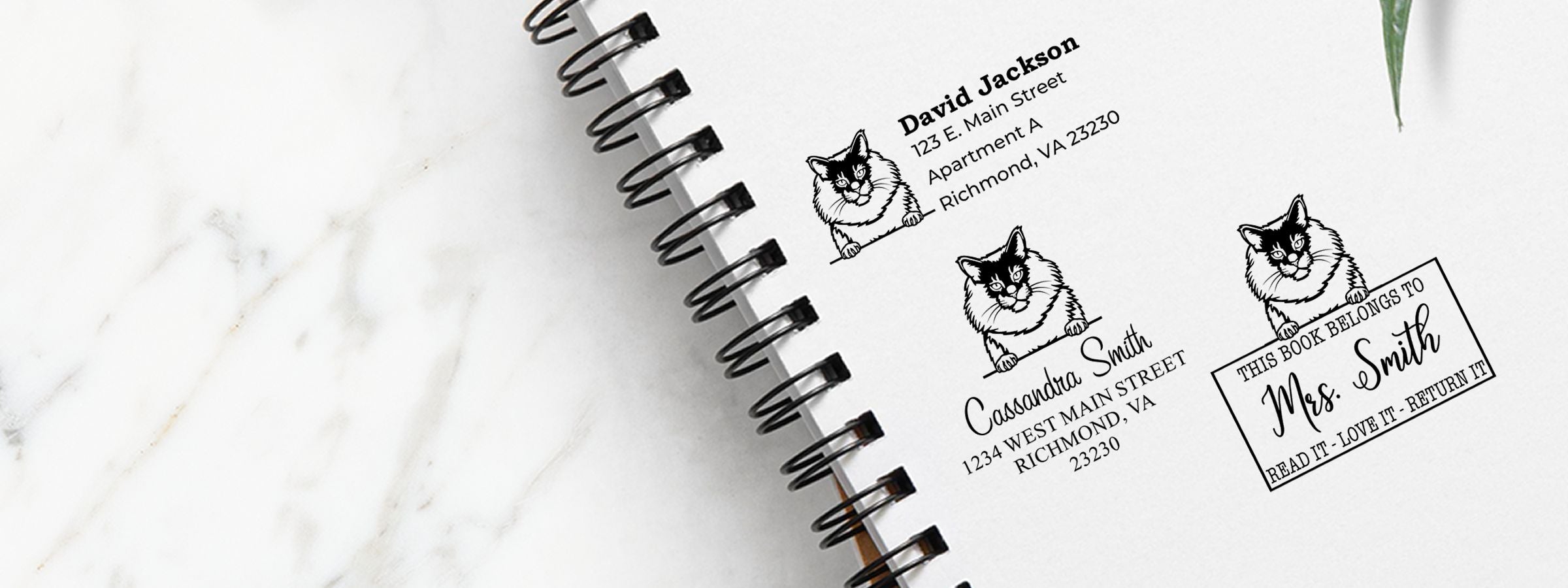 Open spiral notebook on white marble with three cat address stamps, including Mrs. Smith bookplate, for Maine Coon Cat Stamps and Custom Seals.