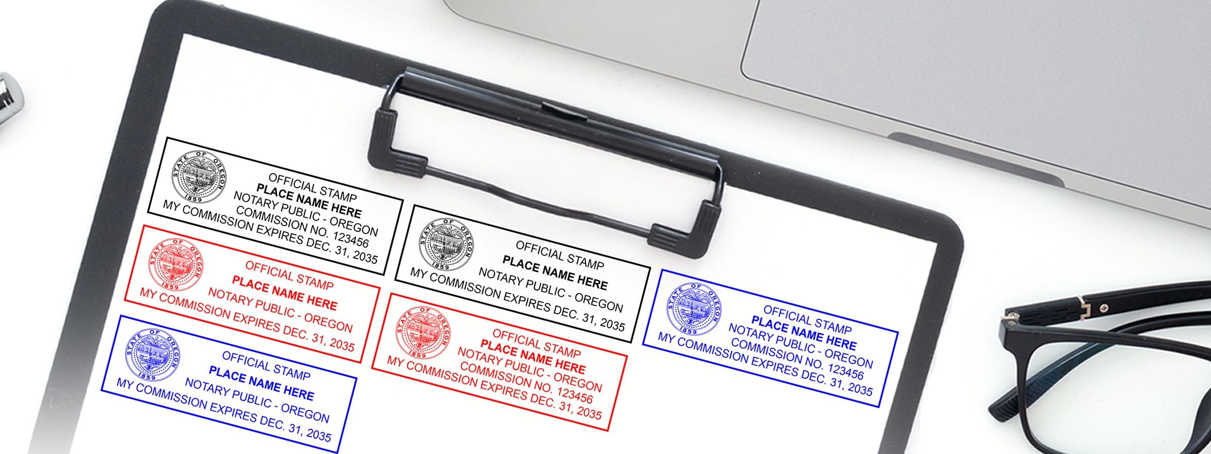 Clipboard with sample notary public stamp designs in black, red, and blue beside a laptop and glasses for Oregon Notary Supplies, Stamps and Seals.