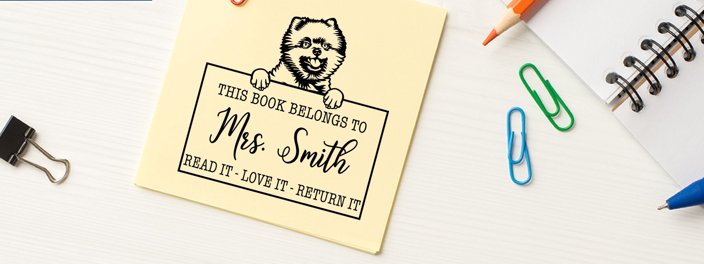 Yellow bookplate sticker with cartoon bear and “This book belongs to Mrs. Smith” on a white desk, for Pomeranian Dog Stamps and Custom Seals.