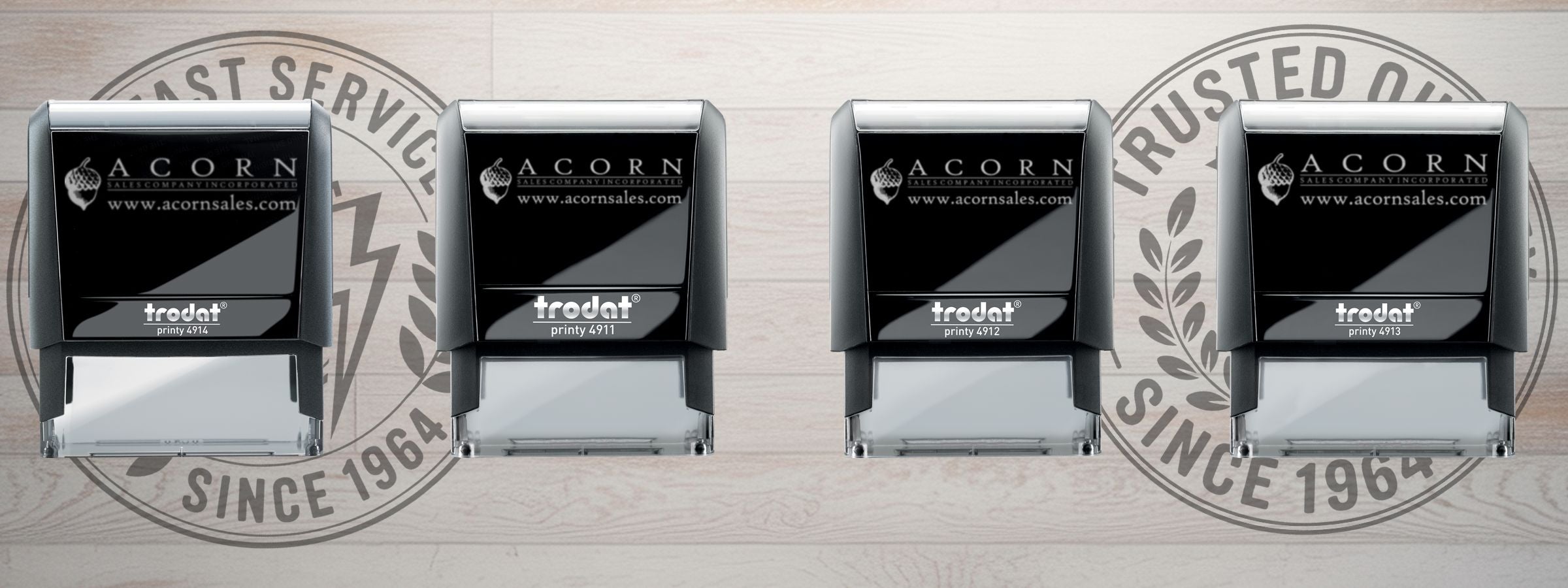 Four black Trodat Self-Inking Custom Stamps branded Acorn Sales Company on light wood with faint Trusted seals.