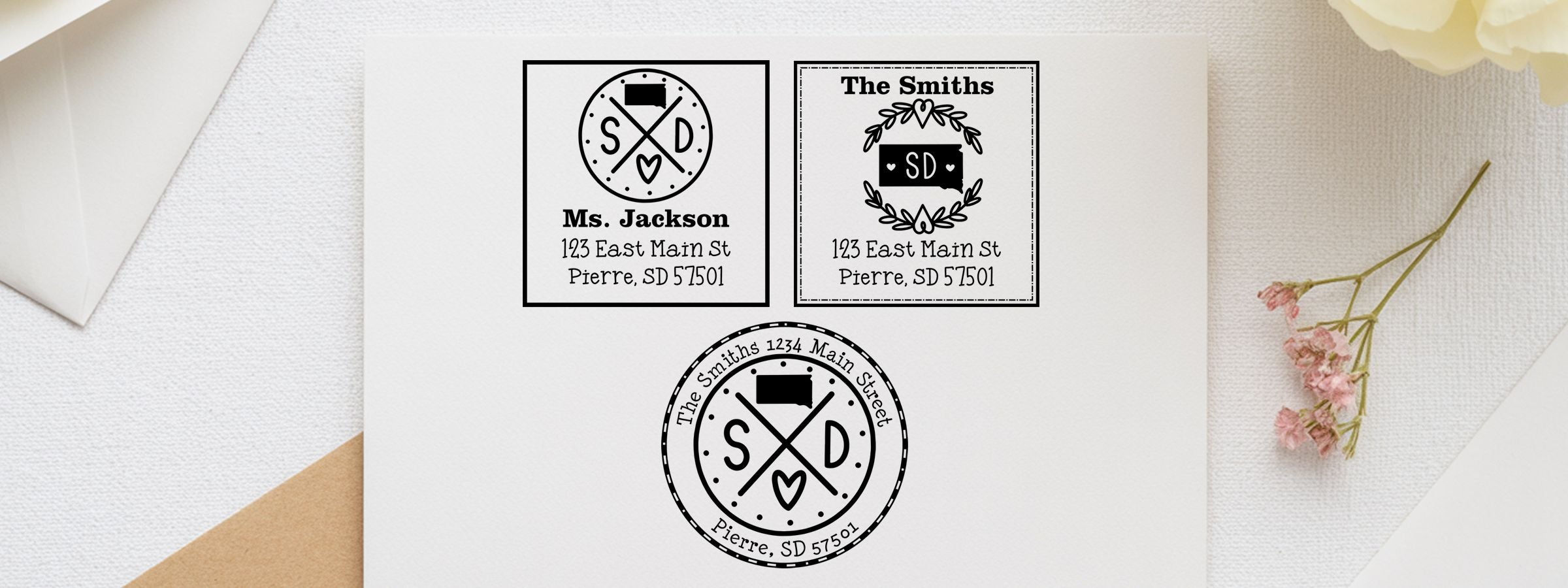 South Dakota Designer Stamps and Seals mockup of three personalized black-and-white address stamps for Ms. Jackson and The Smiths on a white envelope.
