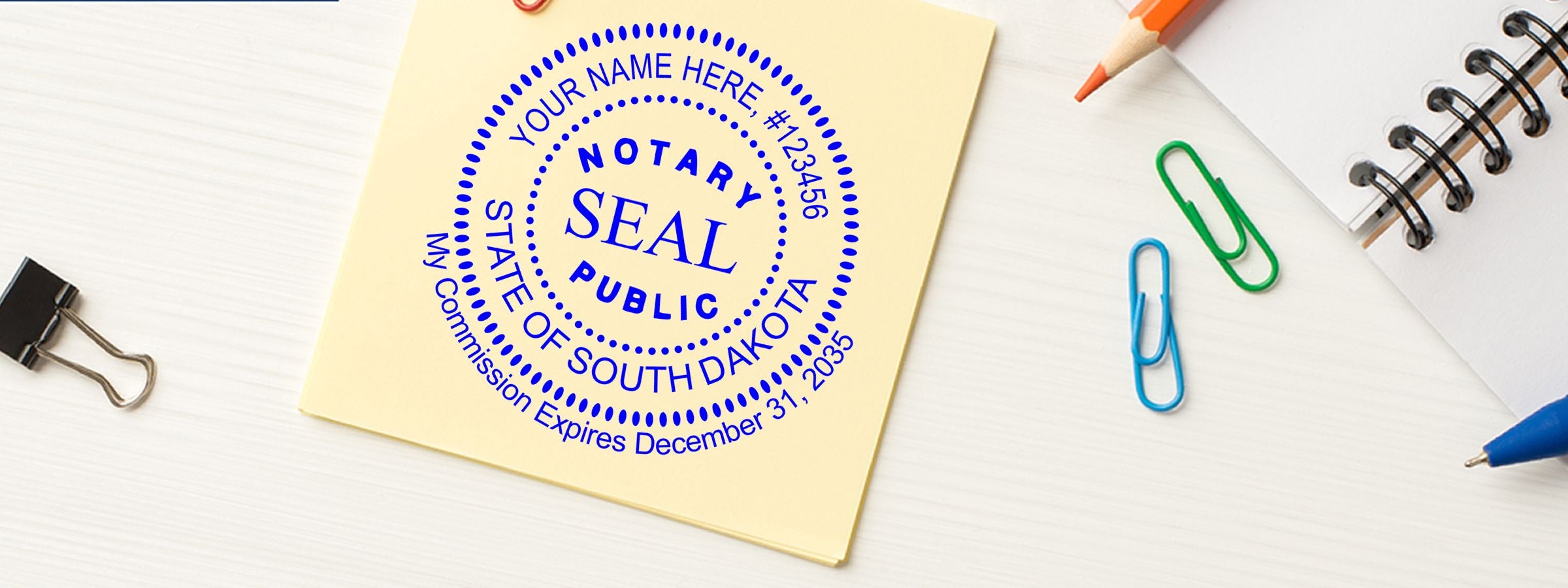 Sticky note with blue South Dakota Notary Seal, paperclips, binder clip, pencil, and notebook. South Dakota Notary Supplies, Stamps and Seals