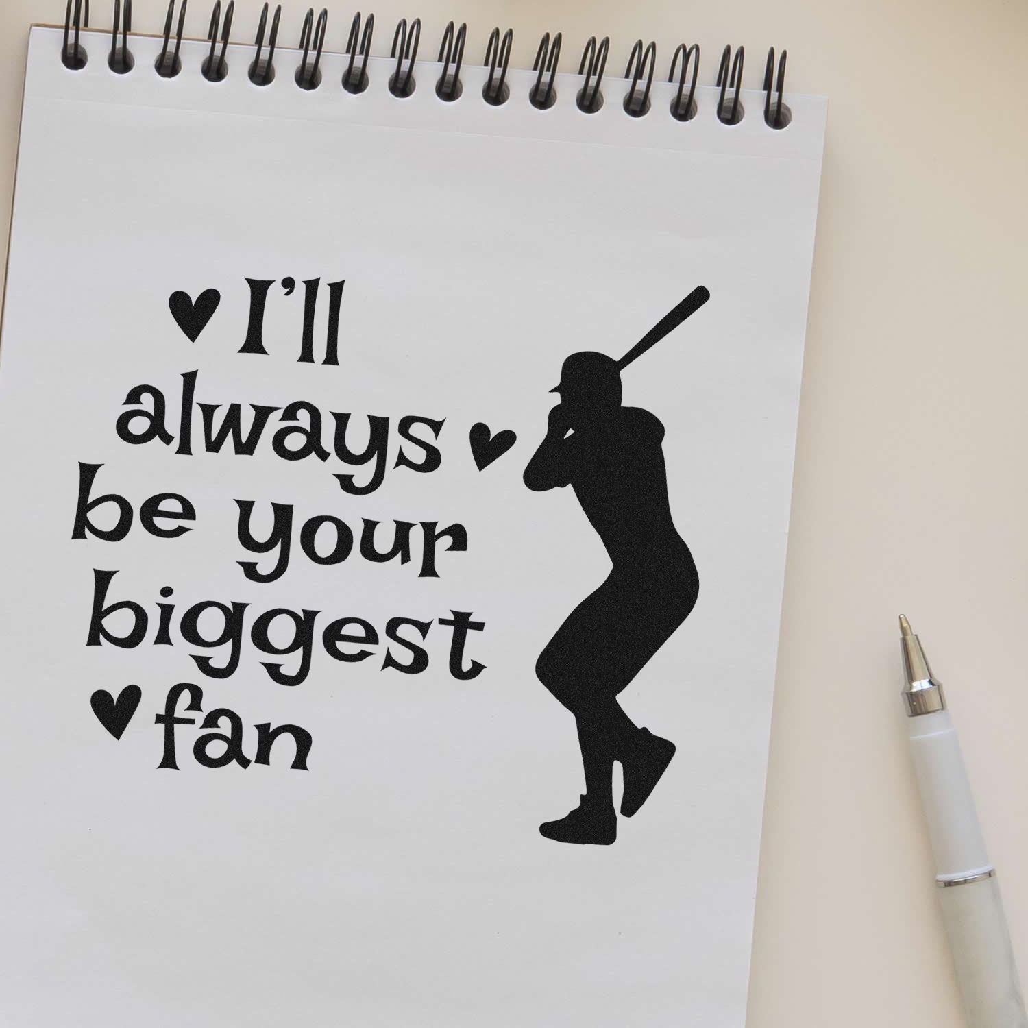 Baseball rubber stamp design with Ill always be your biggest fan quote, hearts, and player silhouette on a notebook page.