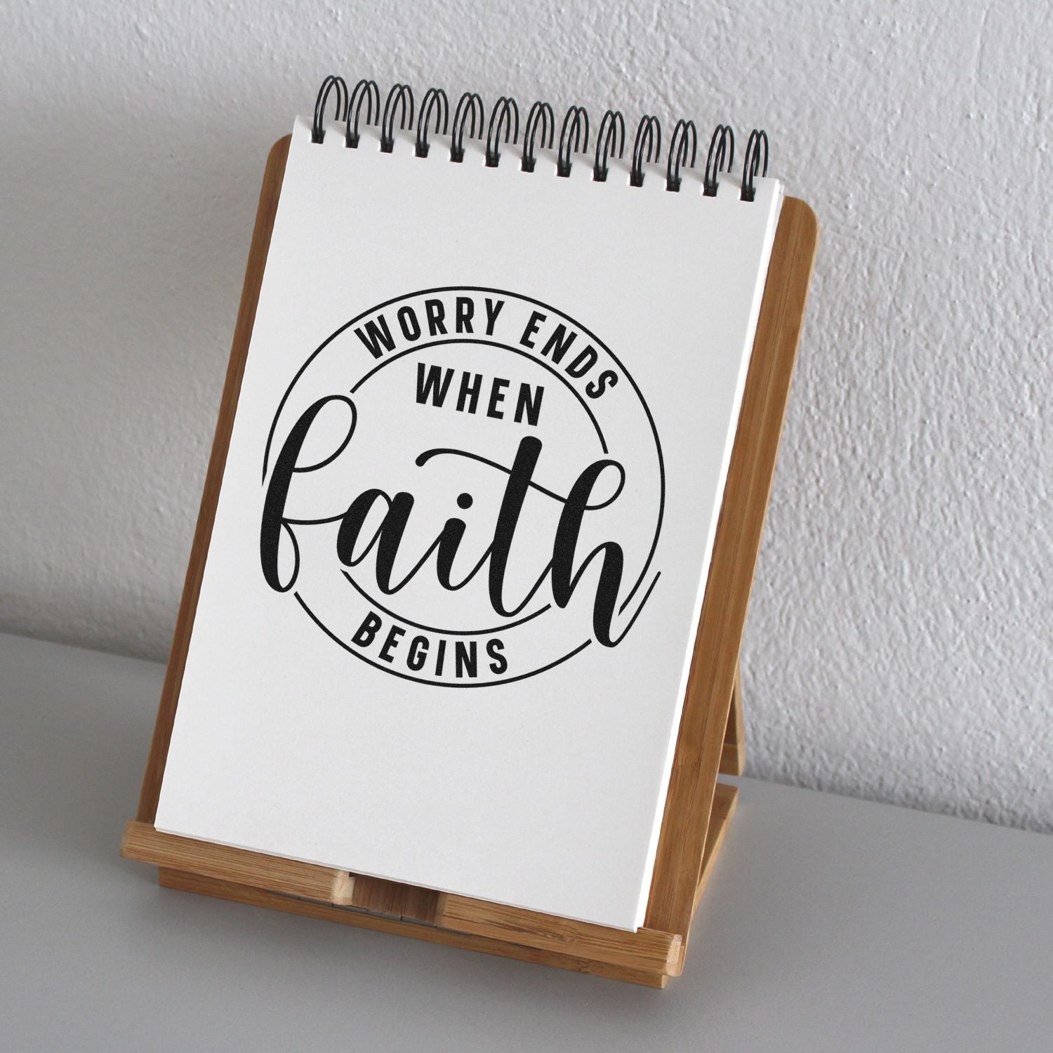 Faith-inspired rubber stamp design reading Worry ends when faith begins on a notepad display stand.