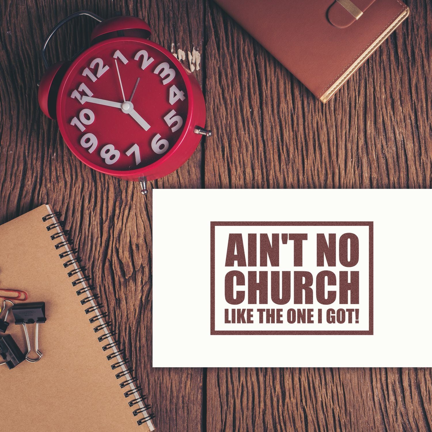 Custom rubber stamp mockup with church slogan Aint No Church Like the One I Got! on a desk.