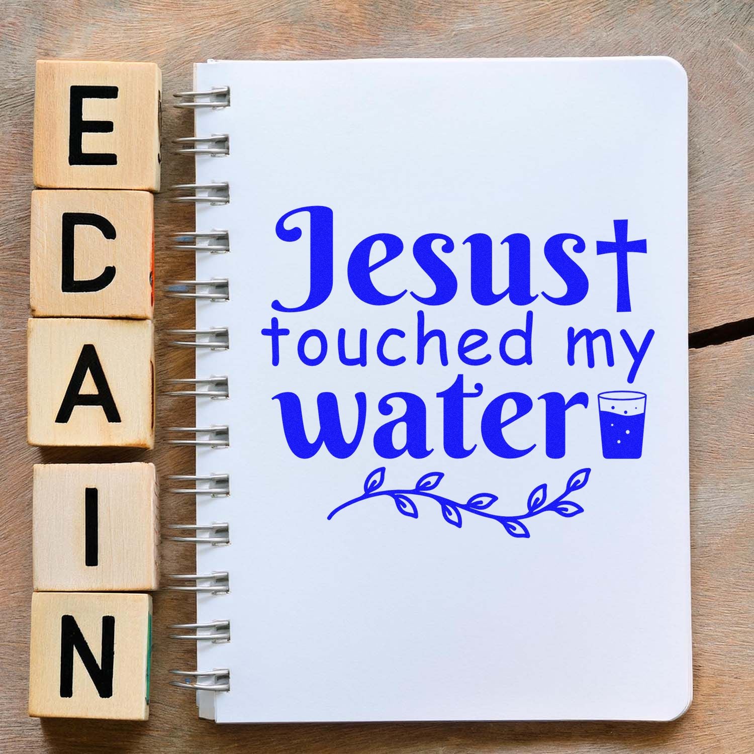 Christian rubber stamp design reading Jesus touched my water on a notebook with wooden alphabet blocks.