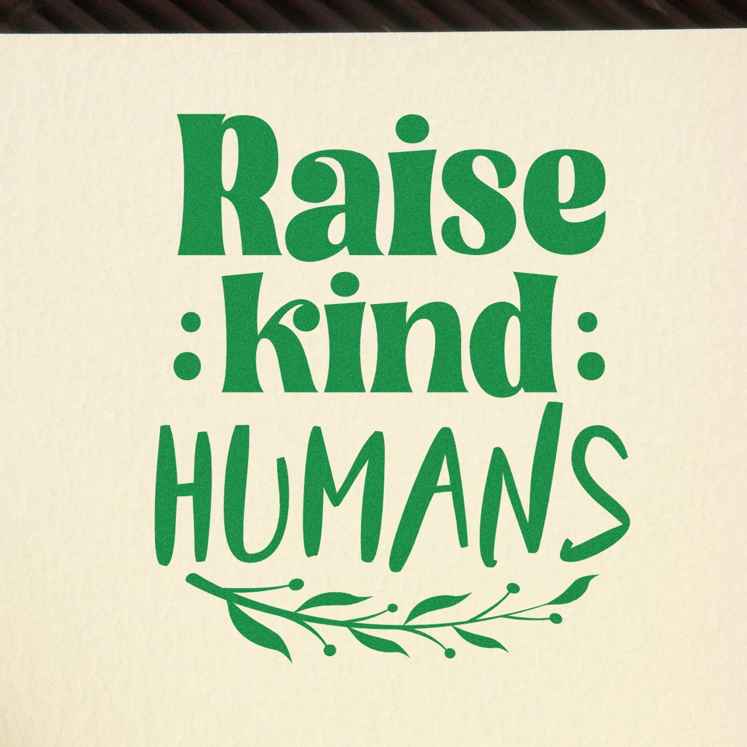 Inspirational rubber stamp design reading Raise Kind Humans with green leaf flourish for teachers and classrooms.