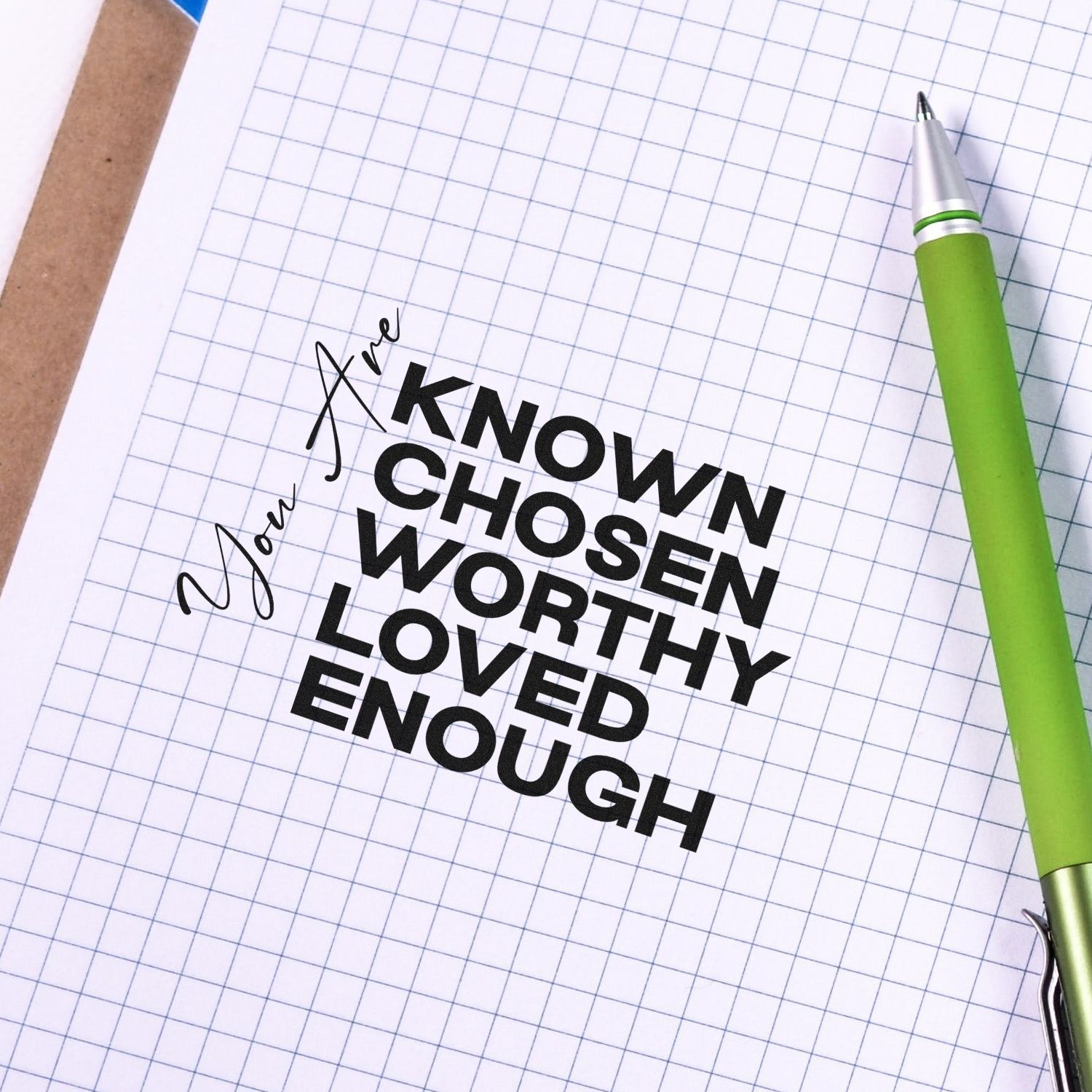 Custom rubber stamp quote design: You are known, chosen, worthy, loved, enough on notebook paper with green pen.