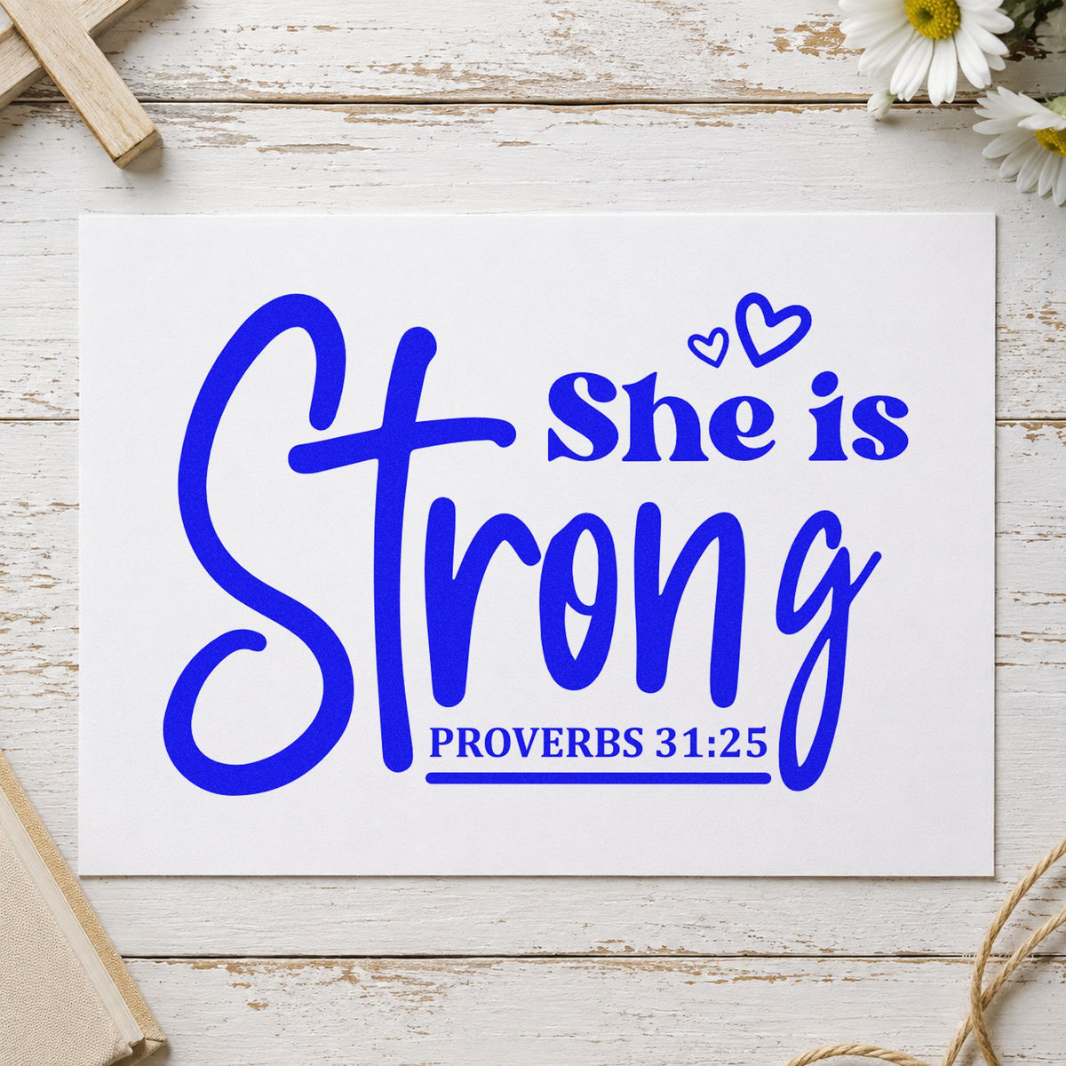 She Is Strong Cross Script craft stamp imprinted in blue ink on paper, a design suited to women's retreat tees.