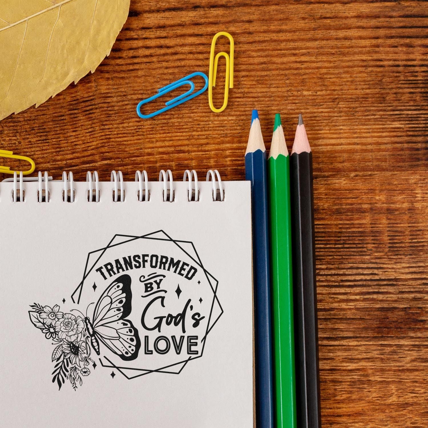 Christian rubber stamp design reading Transformed by Gods Love with butterfly and floral artwork for faith-based crafts.