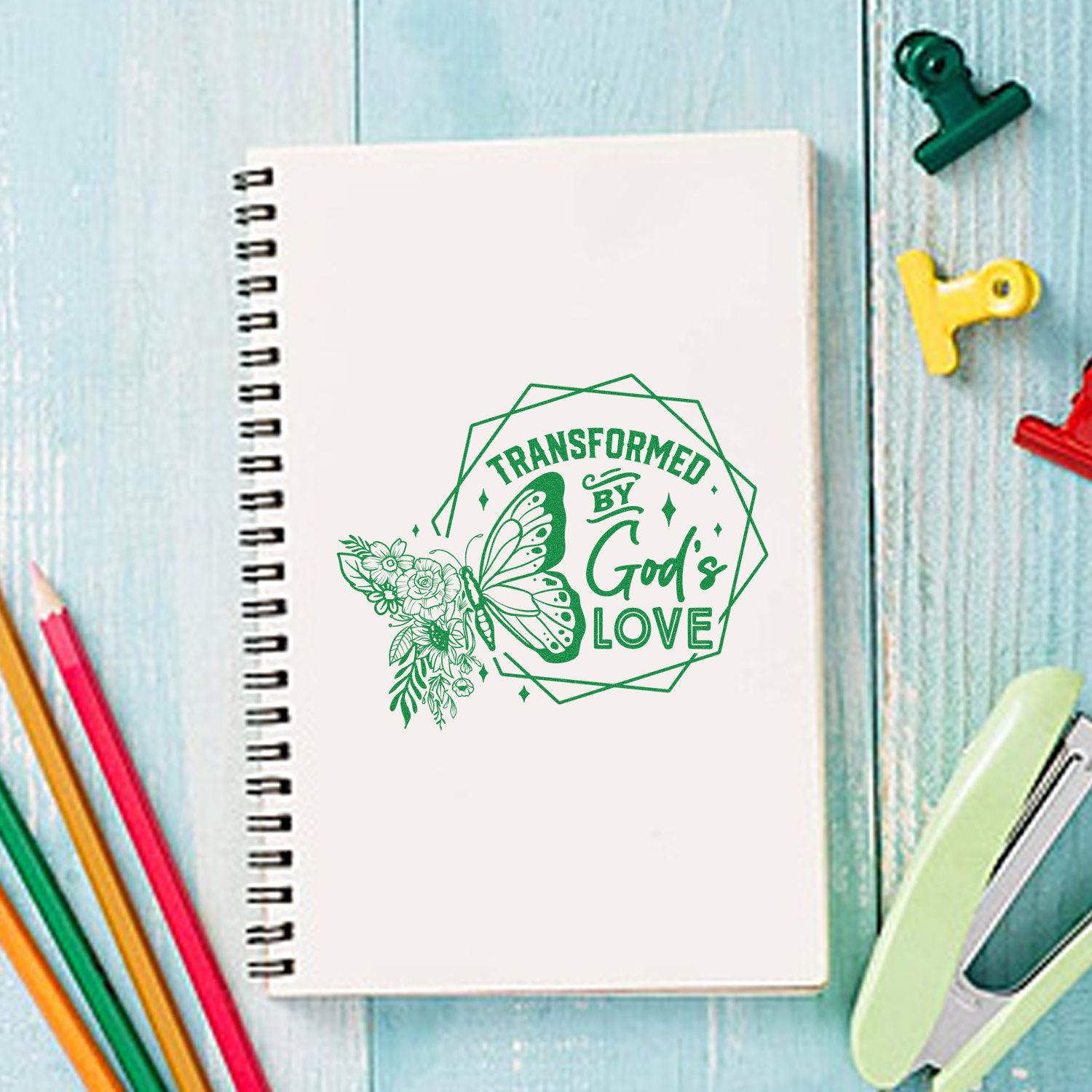 Faith-based butterfly floral rubber stamp design reading Transformed by Gods Love on a spiral notebook.