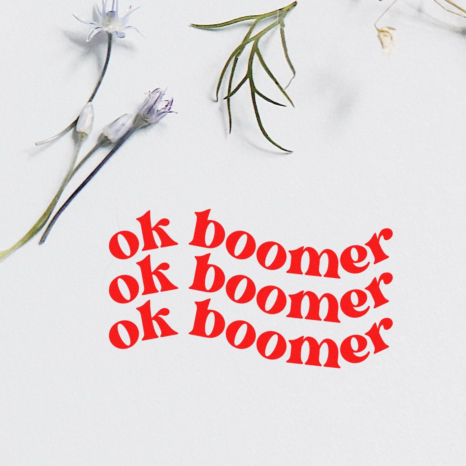Ok boomer rubber stamp impression with bold red text and floral accents for humorous card making and paper crafts.