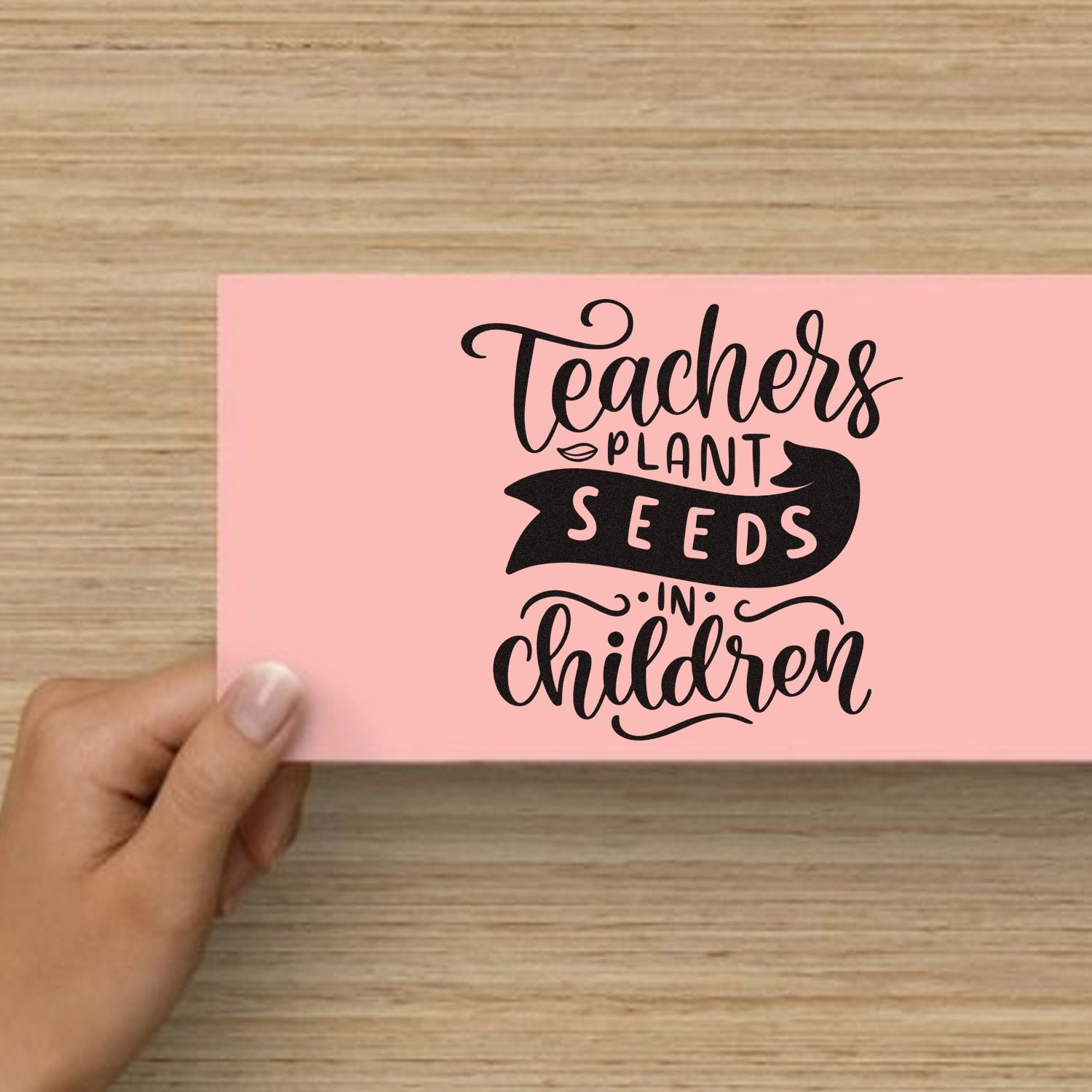 Teacher appreciation rubber stamp design reading Teachers plant seeds in children on pink card held by hand.