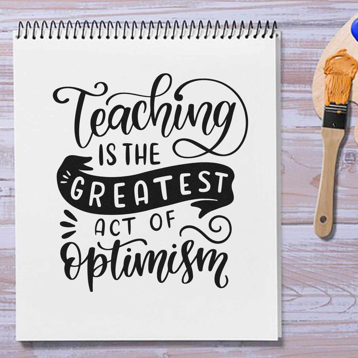 Vintage Pro Teaching Is The Greatest Act Of Optimism Premium Wooden Stamp imprint stamped in black ink. "Teaching Is the Greatest Act of Optimism" combines script, capitals, and a dark ribbon.