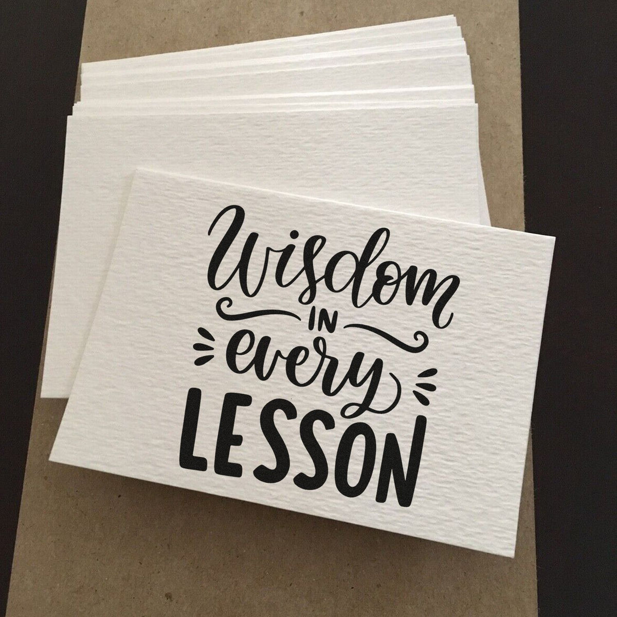 Wisdom In Every Lesson Premium Wooden Stamp - Vintage Pro imprint stamped in black ink. "Wisdom in Every Lesson" pairs flowing script and bold capitals with decorative strokes.