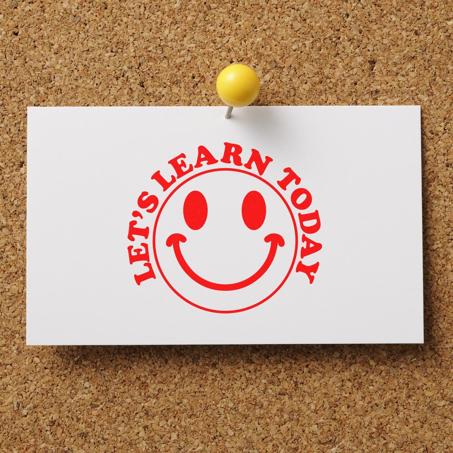Red smiley-face rubber stamp reading Lets Learn Today on white card, pinned to corkboard for classroom motivation.