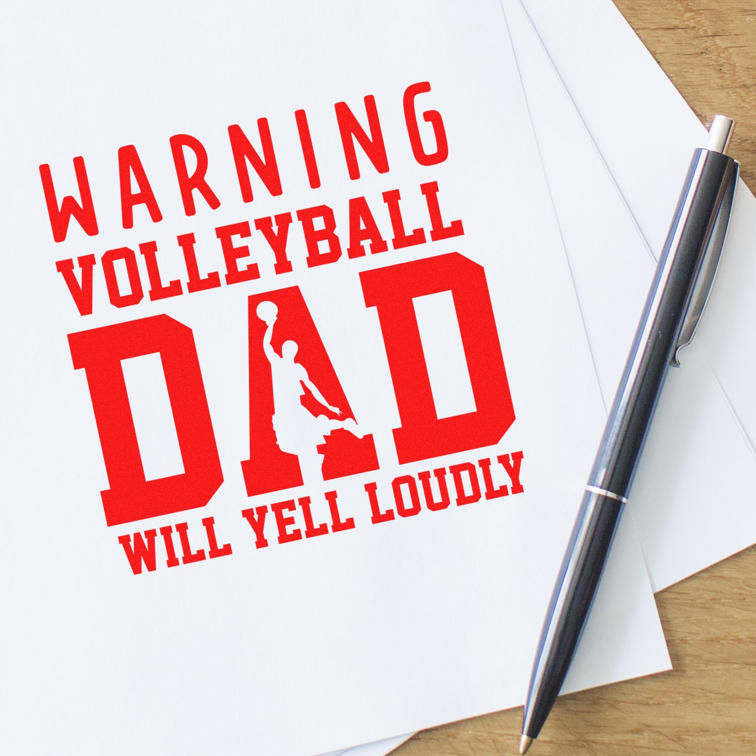 Custom rubber stamp design reading Warning Volleyball Dad Will Yell Loudly in bold red on paper with pen.