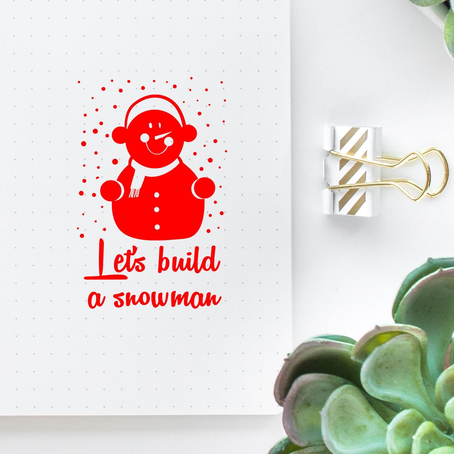 Red snowman rubber stamp design with Lets build a snowman text on a planner page, perfect for holiday crafting.