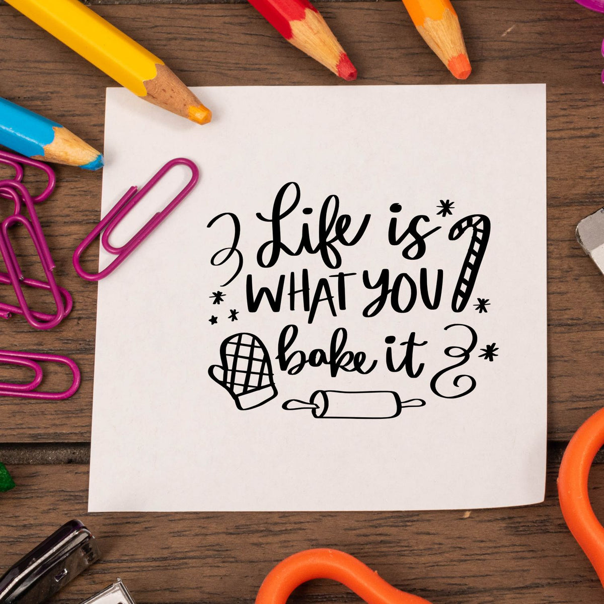Life Is What You Bake Stamp - Premium Vintage Pro Wooden imprint stamped in black ink. "Life Is What You Bake It" features a candy cane, oven mitt, rolling pin, stars, and curls.