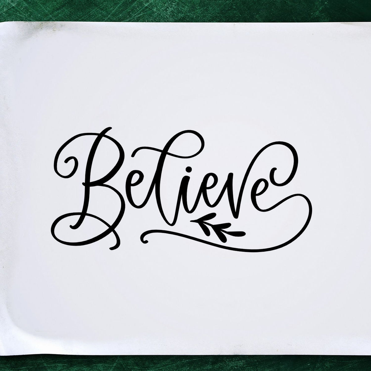 Believe With Leaf Flourished Lettering Premium Wooden Stamp - Vintage Pro imprint stamped in black ink. Elegant script "Believe" features long looping strokes and a small leafy accent.