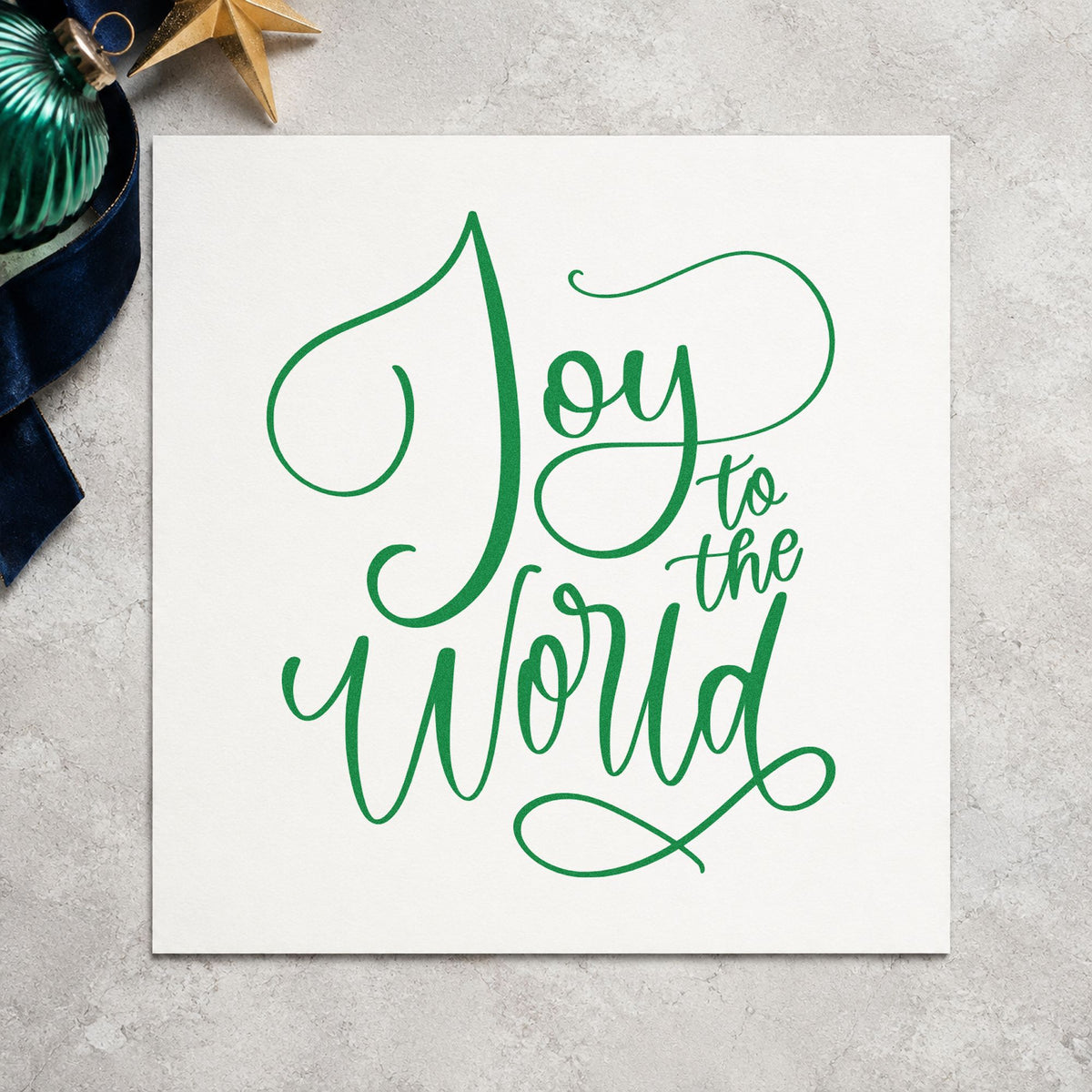 Joy To The World Thin Script craft stamp imprint in green ink on a handmade project, one idea being vellum gift tags.