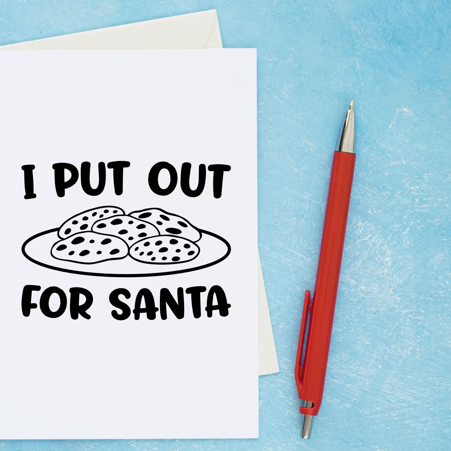 Christmas rubber stamp design reading I Put Out For Santa with cookies illustration on a greeting card and red pen.