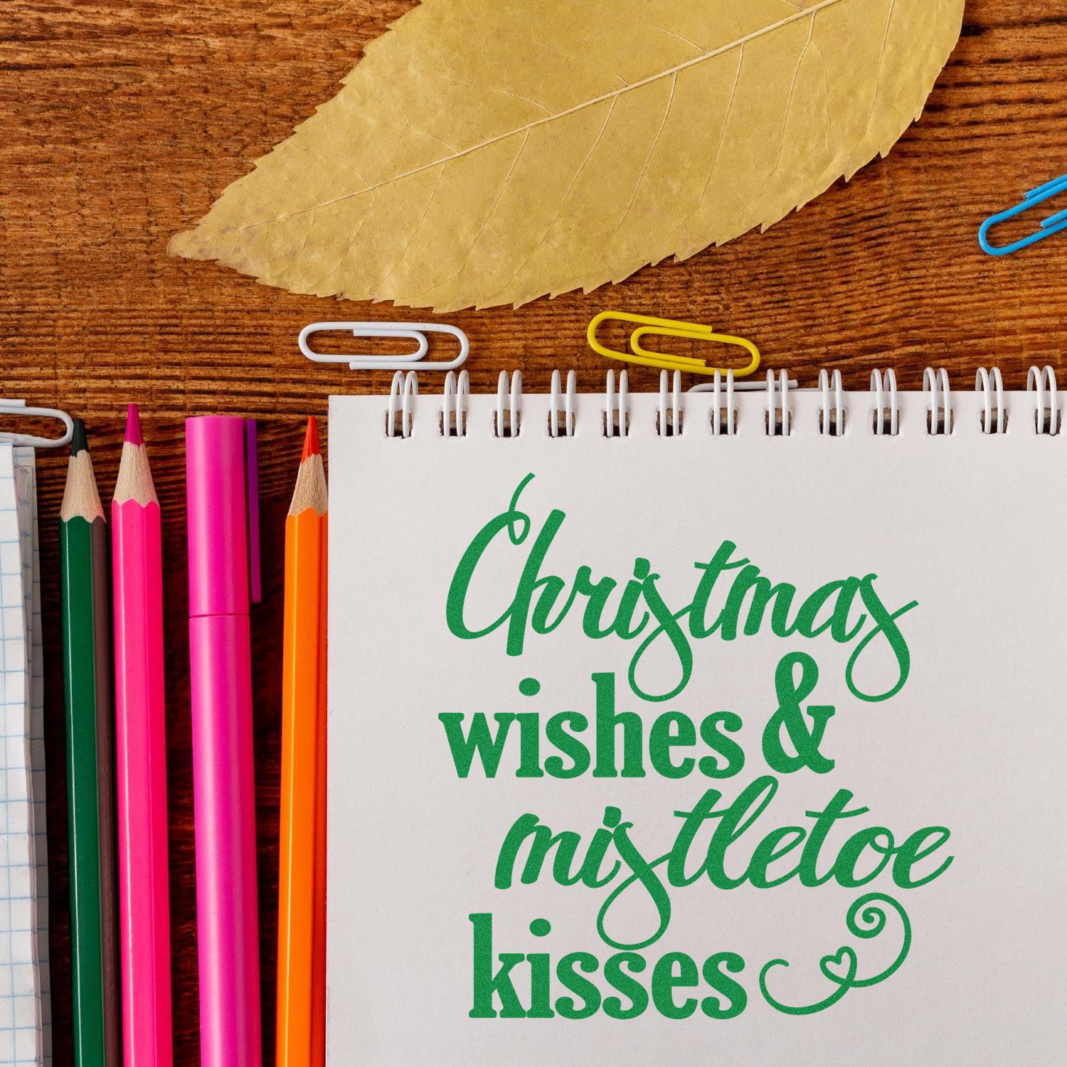 Holiday rubber stamp design reading Christmas wishes & mistletoe kisses on a notebook with colorful pencils.