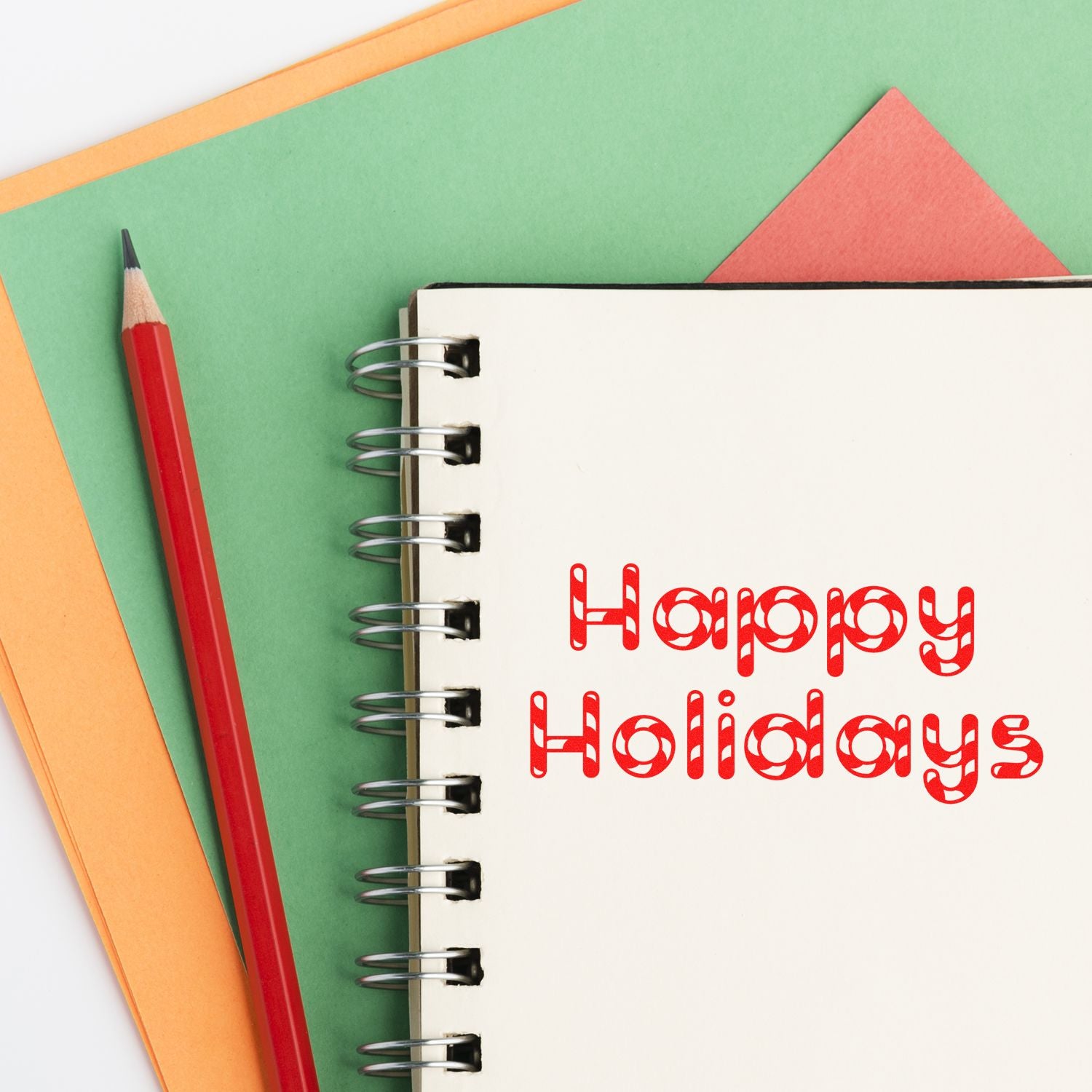 Happy Holidays rubber stamp design on notebook, with pencil and colorful paper for festive cards, scrapbooking, and crafts.