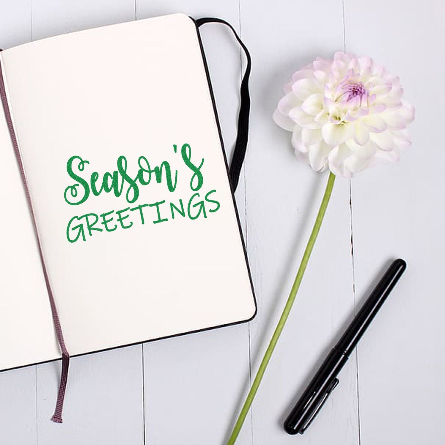 Seasons Greetings rubber stamp design for holiday cards, shown in green script on a notebook page.