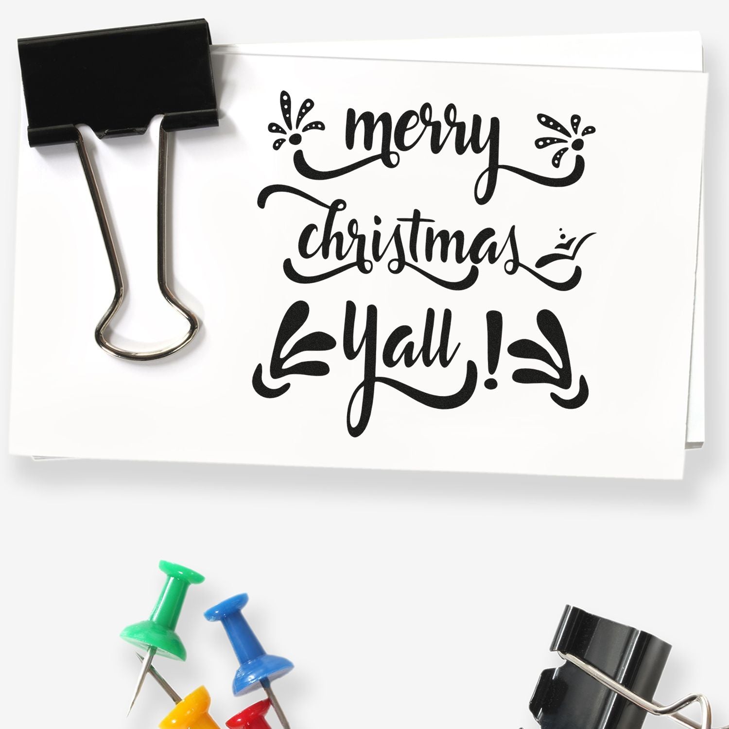 Merry Christmas Y'all rubber stamp design in decorative script, shown clipped to paper with binder clip.