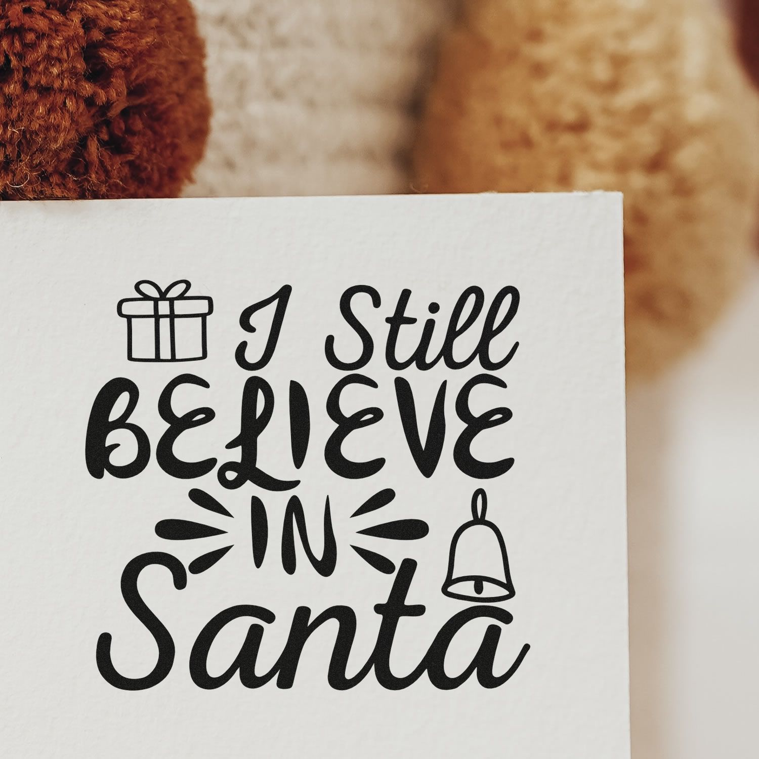 Christmas rubber stamp design reading I Still Believe in Santa with gift and bell icons on white paper.