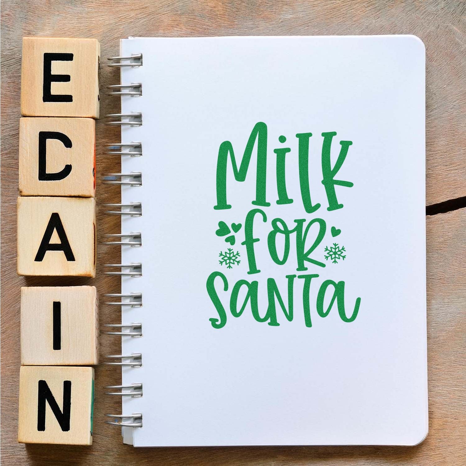 Custom rubber stamps beside a notebook with Milk for Santa holiday lettering, ideal for Christmas craft and card designs.