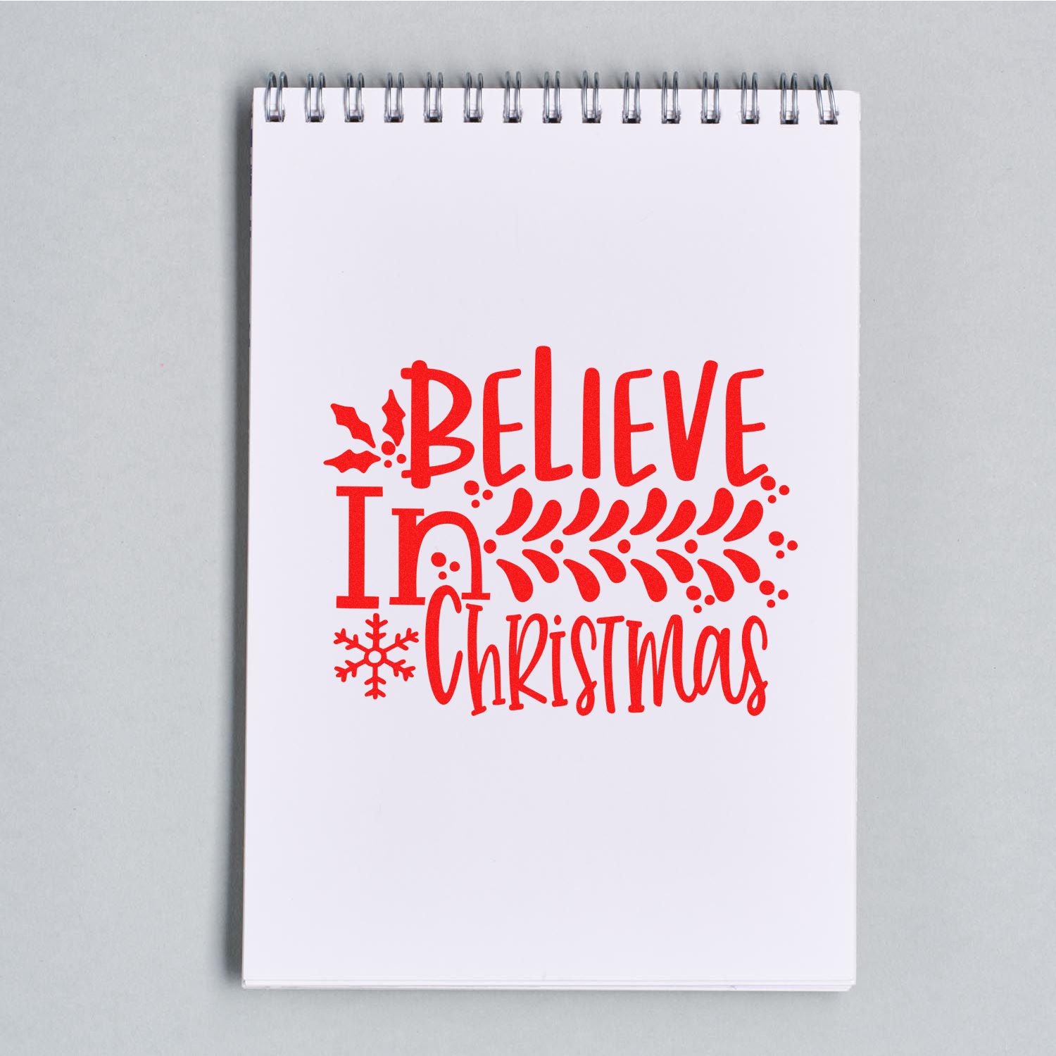 Holiday rubber stamp design with red Believe In Christmas lettering, holly and snowflake for festive cards, gifts, and crafts.