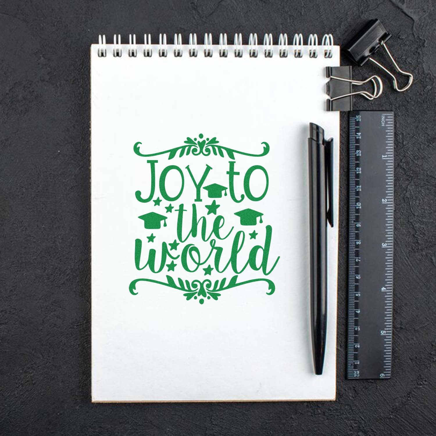 Green Joy to the World graduation rubber stamp design on notebook, perfect for teacher and student crafts.