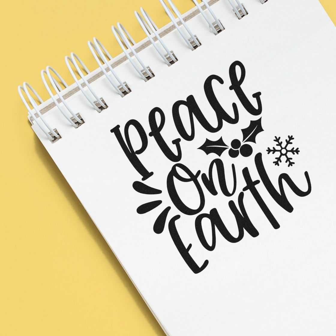 Peace on Earth holiday rubber stamp design with holly and snowflake on a spiral notebook, perfect for Christmas crafts