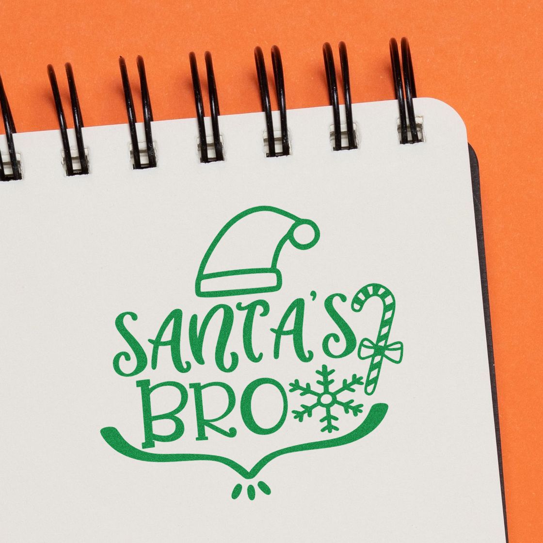 Christmas rubber stamp design reading Santas Bro with Santa hat, candy cane and snowflake on a notebook page.